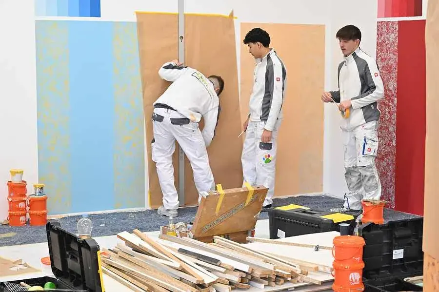 Drei Lehrlinge arbeiten an großen Übungswänden mit Farbflächen